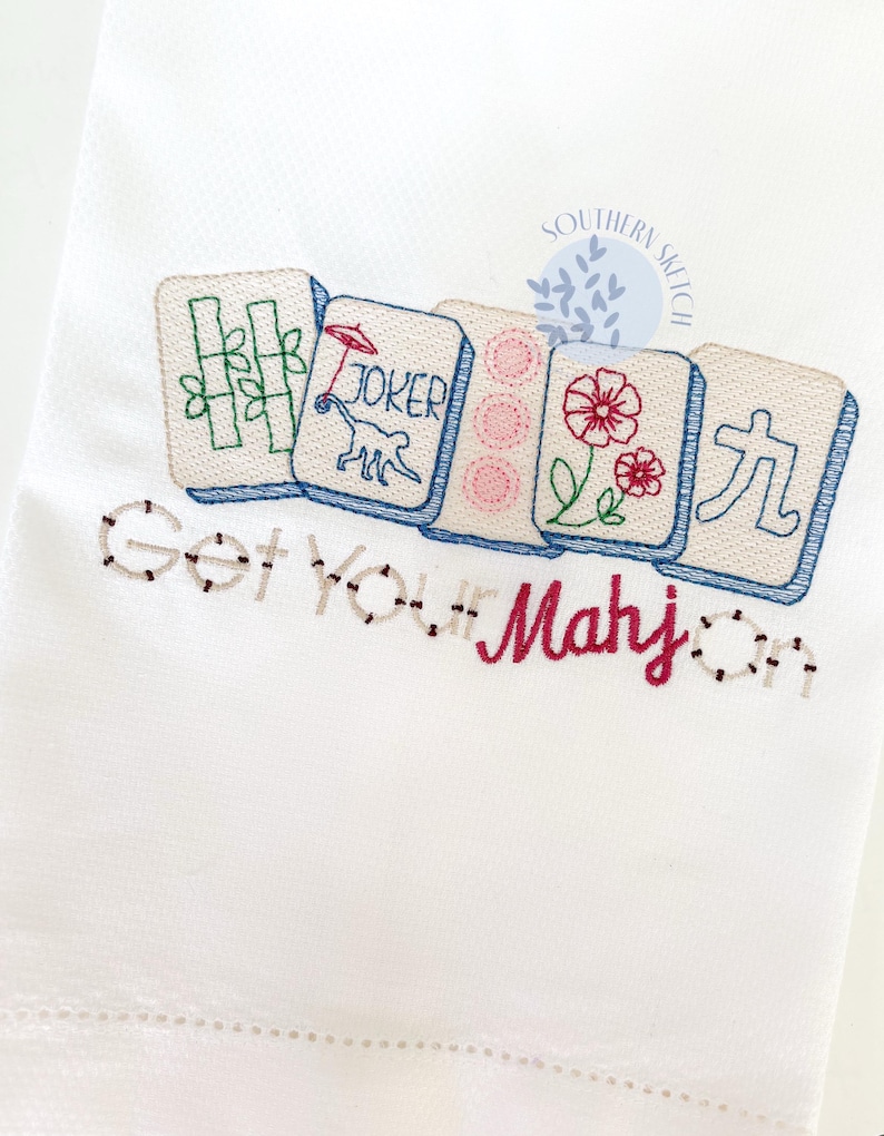 May include: White embroidered towel featuring colorful Mahjong tiles with bamboo, a joker, flowers, and Chinese characters. The text "Get Your Mahj On" is embroidered below the tiles in a playful font.