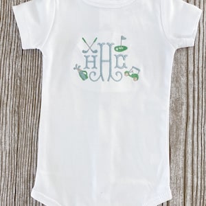May include: White baby onesie with a blue and green embroidered monogram of the letter "H" with golf-themed imagery, including golf clubs, a golf ball, a flag, and a golf cart.