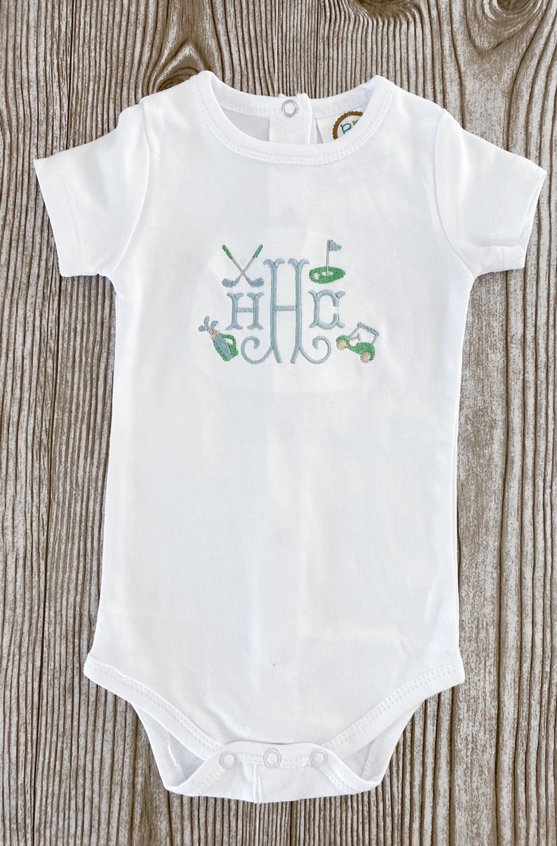 May include: White baby onesie with a blue and green embroidered monogram of the letter "H" with golf-themed imagery, including golf clubs, a golf ball, a flag, and a golf cart.