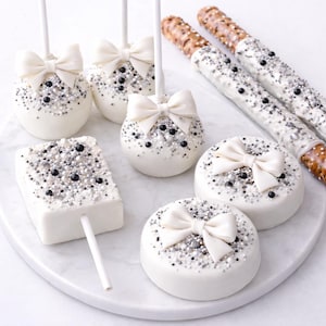 Puede incluir: Una variedad de dulces cubiertos de chocolate blanco, que incluyen cake pops, galletas y pretzels, decorados con chispas plateadas y negras y lazos blancos. Los dulces est&aacute;n dispuestos en una fuente de m&aacute;rmol blanco.