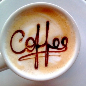 K&ouml;nnte beinhalten: Eine wei&szlig;e Keramiktasse mit einer braunen Fl&uuml;ssigkeit und dem Wort "Coffee" in Schokoladensauce geschrieben.