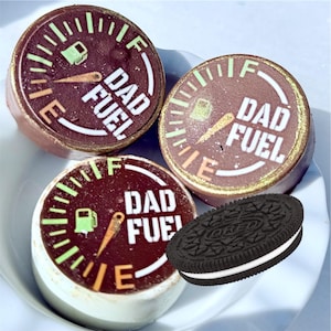 May include: A plate holds three round chocolate treats with a gauge design and the words "DAD FUEL" in white. The gauge shows a fuel tank and needle. An Oreo cookie sits next to the treats.