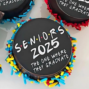 Pu&ograve; includere: Una torta rotonda nera decorata con confettini colorati e il testo "Seniors 2025 The One Where They Graduate".