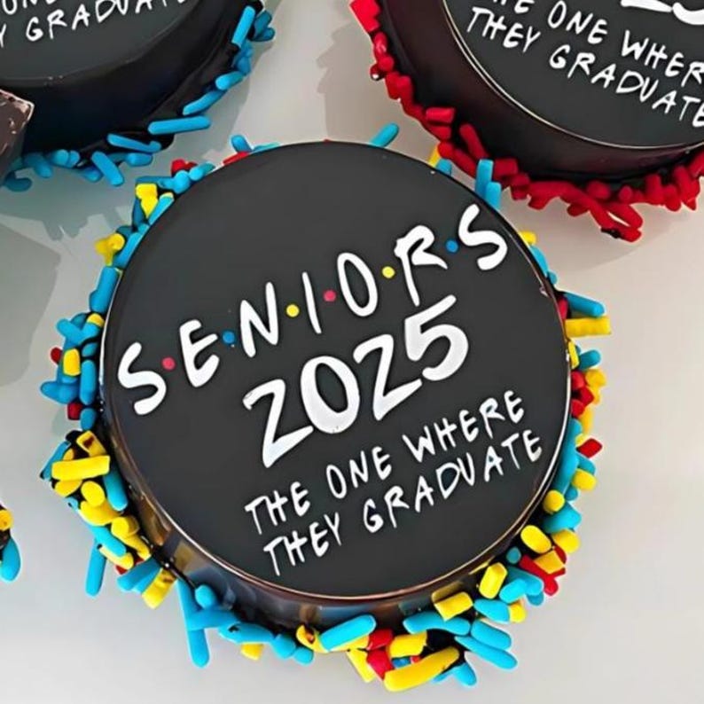 Pu&ograve; includere: Una torta rotonda nera decorata con confettini colorati e il testo "Seniors 2025 The One Where They Graduate".