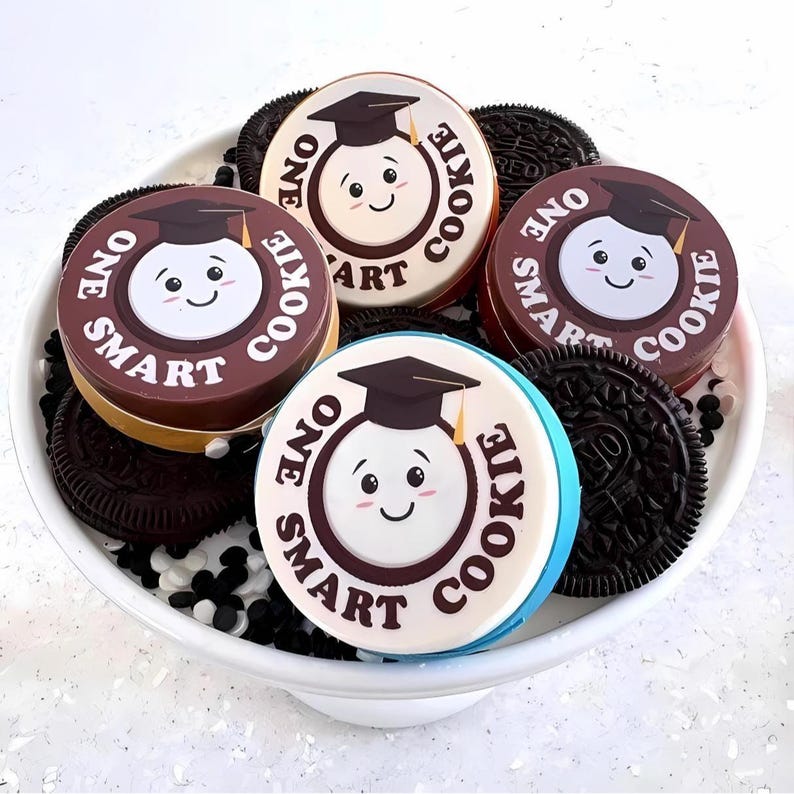 May include: A white bowl filled with chocolate chip cookies decorated with graduation caps and the text "One Smart Cookie".