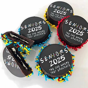 Pu&ograve; includere: Quattro biscotti rotondi neri e bianchi con codette. Ogni biscotto &egrave; decorato con il testo "SENIORS 2025 THE ONE WHERE THEY GRADUATE".