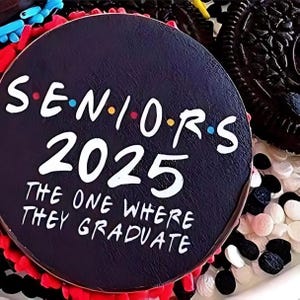 Pu&ograve; includere: Una torta rotonda nera con glassa bianca e il testo "Seniors 2025 The One Where They Graduate" in bianco. La torta &egrave; decorata con codette colorate.
