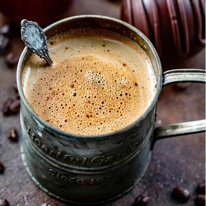 K&ouml;nnte beinhalten: Nahaufnahme einer vintage Metalltasse gef&uuml;llt mit schaumigem Kaffee. Die Tasse tr&auml;gt die Aufschrift "Heartful Garden" und "Since 197".