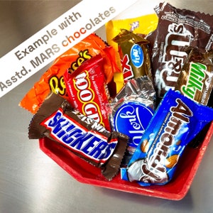 K&ouml;nnte beinhalten: Eine Auswahl an Schokoladenriegeln in einer roten sechseckigen Sch&uuml;ssel. Die Riegel umfassen Snickers, 100 Grand, Almond Joy, Milky Way, York Peppermint Patties und Reese's Peanut Butter Cups.