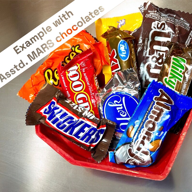 K&ouml;nnte beinhalten: Eine Auswahl an Schokoladenriegeln in einer roten sechseckigen Sch&uuml;ssel. Die Riegel umfassen Snickers, 100 Grand, Almond Joy, Milky Way, York Peppermint Patties und Reese's Peanut Butter Cups.