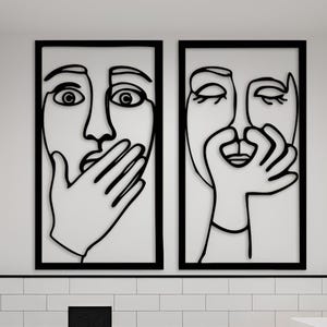 May include: Modern bathroom with white subway tile walls and a dark gray floor. Two framed black line art pieces hang above the toilet. A wooden vanity with a white rectangular sink and black faucet is on the right.
