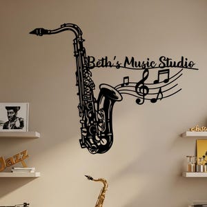 Könnte beinhalten: Ein goldfarbenes Saxophon auf einem schwarzen Ständer, mit einem schwarzen Saxophon-Wandkunstwerk und dem Text "Beth's Music Studio". Der Raum verfügt außerdem über Regale mit Jazzplatten und einen Plattenspieler.