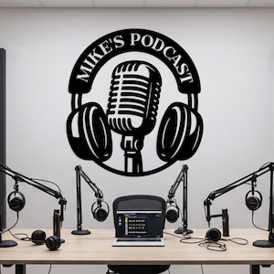 Puede incluir: Una pieza de arte mural de metal negro que dice "Mike's Podcast" con un diseño de micrófono y auriculares. La imagen muestra una configuración de estudio de podcast con un escritorio, micrófonos, auriculares, una computadora portátil y una silla.