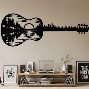 Puede incluir: Arte mural de metal negro con forma de guitarra que representa un paisaje con árboles, un lago y una silueta de ciudad. La obra de arte está montada en una pared beige. El clavijero de la guitarra se extiende hacia la derecha.