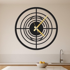 May include: A black, circular wall clock with a target design. The clock has gold-colored hands and is mounted on a light-colored wall. The clock is above a kitchen island with two bar stools.