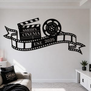 May include: A black metal wall art piece featuring a film clapperboard with the text SMITH'S CINEMA, a film reel, and a strip of film with the text EST. 2025. The design is a horizontal arrangement of cinema-themed icons mounted on a wall.