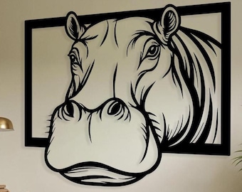 May include: A black and white hippo wall art piece. The hippo's head is framed in a black rectangular border, with the hippo's features detailed in black lines. The hippo appears to be emerging from the wall, creating a 3D effect. The art is mounted on a beige wall.