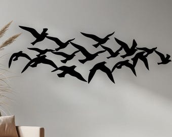 Puede incluir: Una obra de arte mural de metal negro que representa una bandada de pájaros en vuelo. Los pájaros están montados en una pared blanca, creando una estética minimalista y moderna. La obra de arte añade un toque de decoración inspirada en la naturaleza a la habitación.