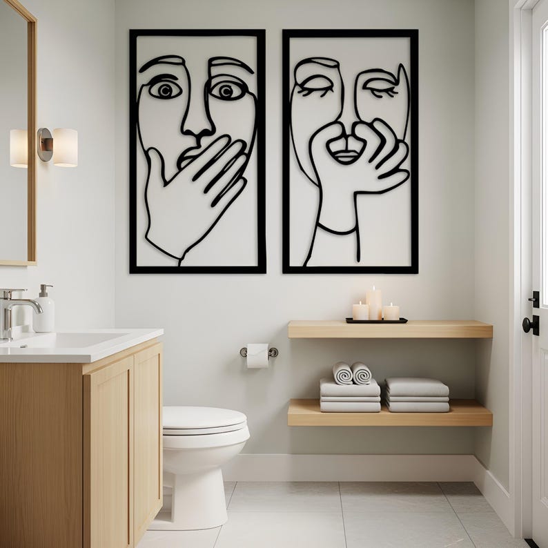 May include: Two framed abstract face art pieces with black outlines on a white background. One face has a hand over its mouth, the other touches its face. The art hangs above a wooden shelf with candles and towels in a bathroom setting.