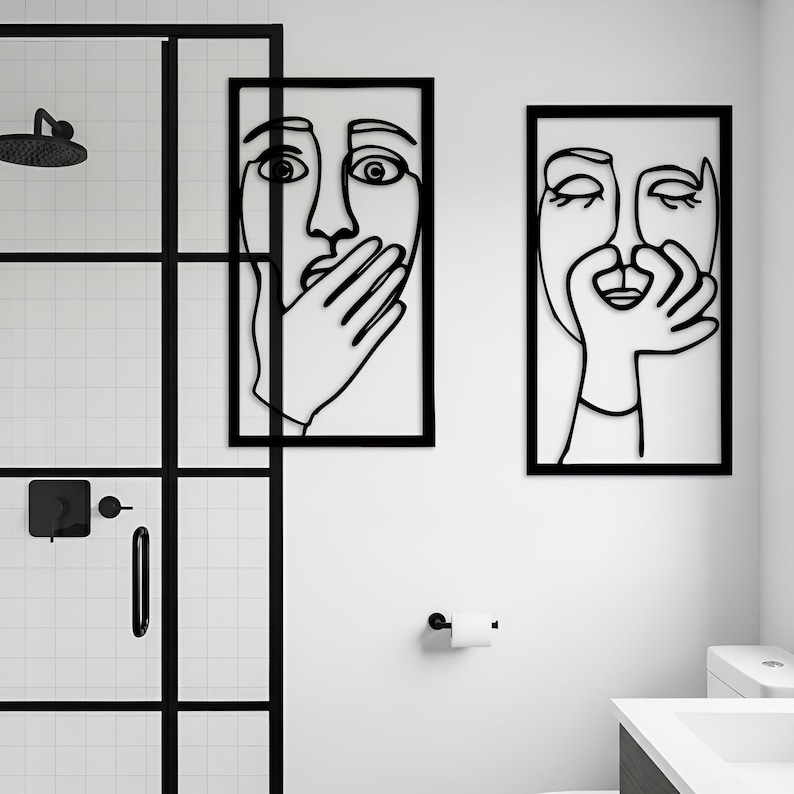 May include: Two framed wall art pieces with black line drawings of faces. One face has a hand covering the mouth, the other has a hand near the mouth. The art is displayed in a modern bathroom setting with a black shower door.