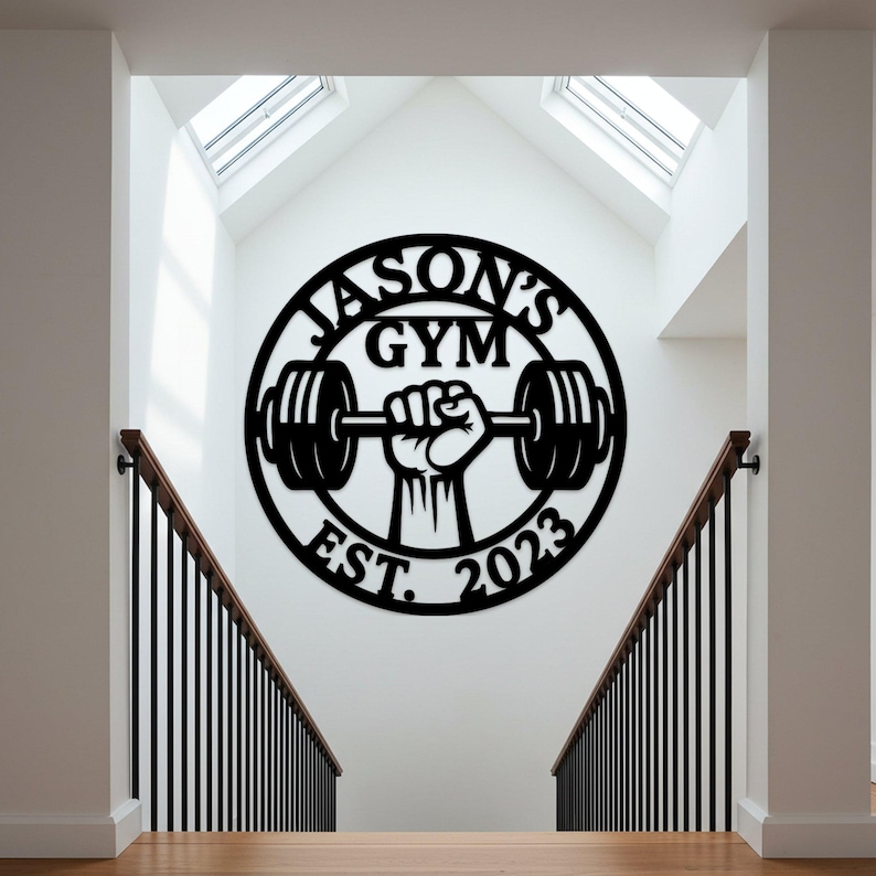 May include: Black metal wall art with the text "JASON'S GYM EST. 2023" in a circular design. The design features a hand holding a barbell. The art is mounted on a white wall above a staircase.