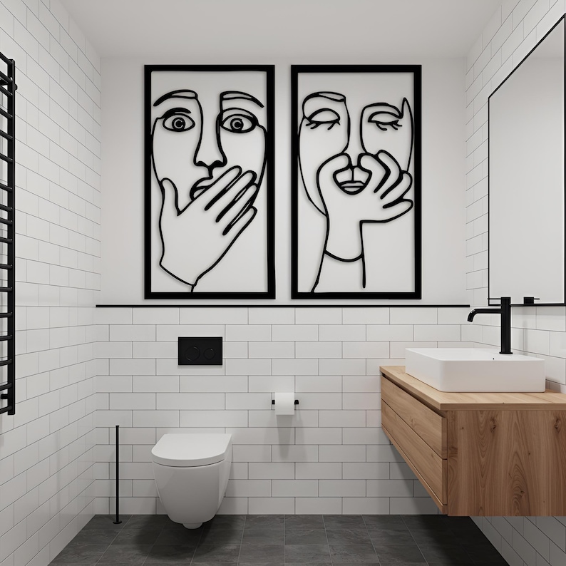 May include: Modern bathroom with white subway tile walls and a dark gray floor. Two framed black line art pieces hang above the toilet. A wooden vanity with a white rectangular sink and black faucet is on the right.