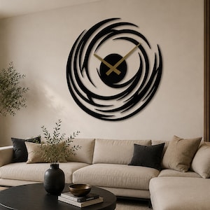 Op de afbeelding: Een grote, moderne wandklok met een zwart, wervelend ontwerp. De wijzers zijn goudkleurig en de wijzerplaat is een effen zwarte cirkel. De klok is bevestigd aan een lichtgekleurde muur, boven een beige bank.