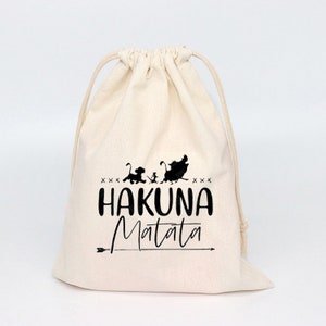 Puede incluir: Una bolsa de algodón blanco con cordón con una silueta negra de los personajes de El Rey León y el texto "Hakuna Matata" impreso en ella.