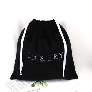 以下が含まれることがあります： 白い紐と「LYXERY BY SWEDEN」という白い刺繍が施された黒い巾着袋です。