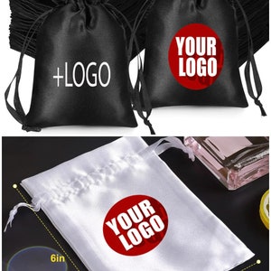 May include: Black and white satin drawstring bags with the text "+LOGO" and "YOUR LOGO" printed on them. The white bag measures 6 inches by 4 inches. These bags are ideal for packaging small gifts or merchandise.