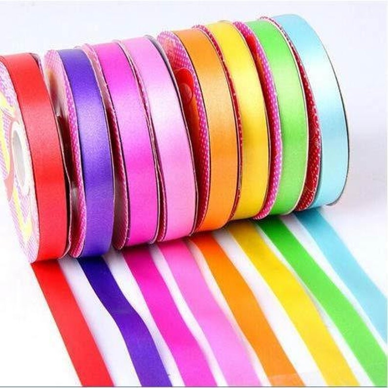 May include: A collection of colorful satin ribbons in a rainbow of hues, including red, purple, pink, orange, yellow, green, and blue. The ribbons are rolled on spools, with the ends of the ribbons extending out. Perfect for crafting and gift wrapping.