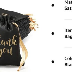 May include: Black satin drawstring bags with gold "thank you" text. The bags have gold ribbon drawstrings and are stacked in a pile. These small bags are ideal for party favors, gifts, or small retail items.