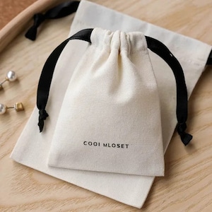May include: A white cotton drawstring bag with black drawstrings and the text "COOOI MLOSET" printed on the front.