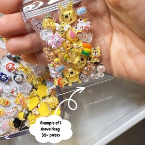 Pu&ograve; includere: Un sacchetto di plastica trasparente pieno di piccole figurine di personaggi dei cartoni animati colorati. Il sacchetto &egrave; etichettato "Esempio di 1 pala/sacchetto 30+ pezzi".