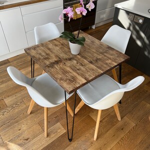 May include: A square wooden dining table with black hairpin legs and four white chairs. A potted pink orchid sits in the center of the table.