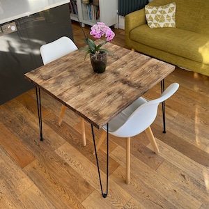 May include: A square wooden table with a rustic finish and black hairpin legs. The table is set with a white chair and a potted orchid plant.