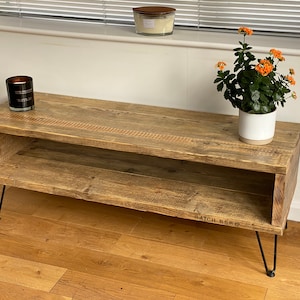 Puede incluir: Un soporte de TV de madera r&uacute;stica con un estante y patas de horquilla. El soporte est&aacute; hecho de madera recuperada y tiene un acabado natural. Tiene 120 cm de ancho y 40 cm de profundidad. El soporte est&aacute; sobre un suelo de madera dura.