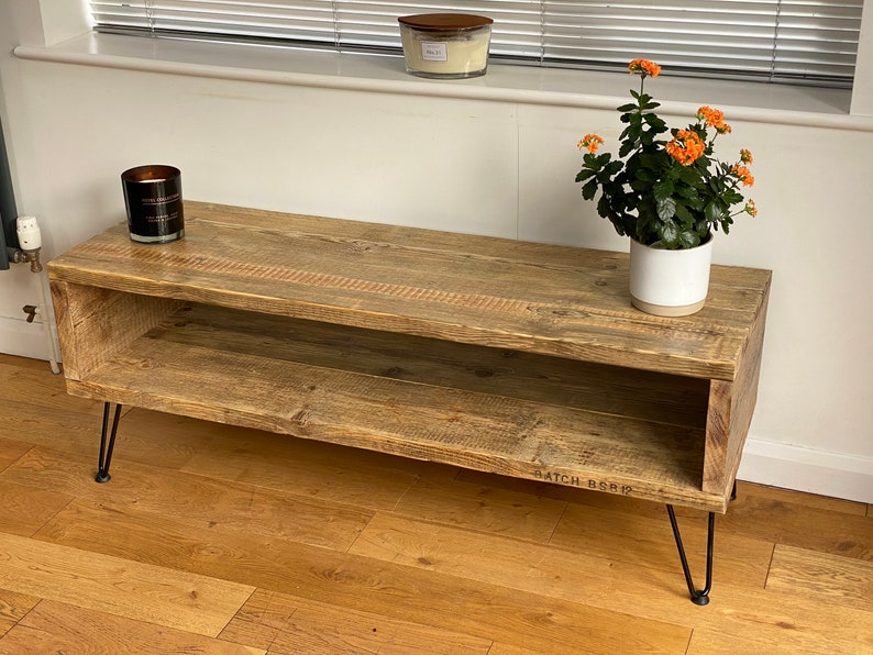 Puede incluir: Un soporte de TV de madera r&uacute;stica con un estante y patas de horquilla. El soporte est&aacute; hecho de madera recuperada y tiene un acabado natural. Tiene 120 cm de ancho y 40 cm de profundidad. El soporte est&aacute; sobre un suelo de madera dura.