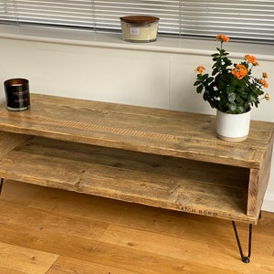 Puede incluir: Una mesa de centro de madera r&uacute;stica con un estante inferior y patas de horquilla negras. La mesa est&aacute; hecha de madera recuperada y tiene un acabado natural. La mesa mide 120 cm de largo y 48 cm de ancho.