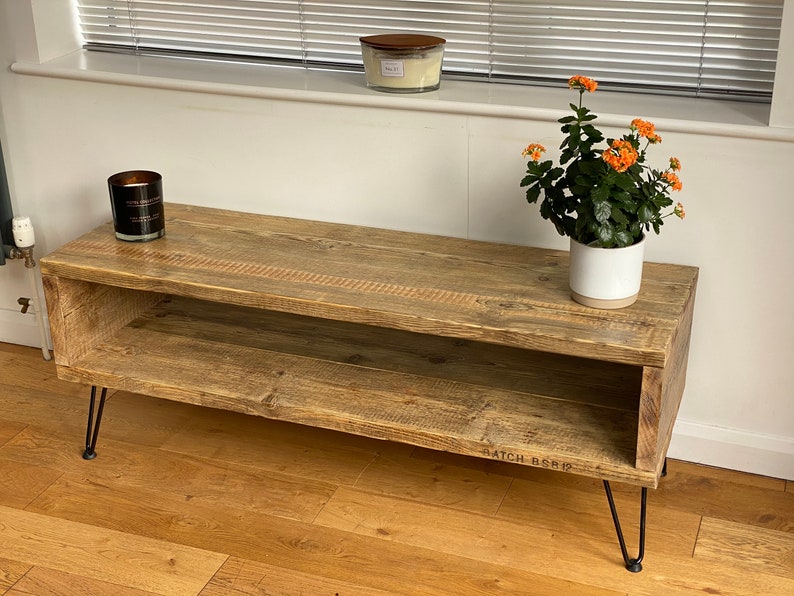 Puede incluir: Una mesa de centro de madera r&uacute;stica con un estante inferior y patas de horquilla negras. La mesa est&aacute; hecha de madera recuperada y tiene un acabado natural. La mesa mide 120 cm de largo y 48 cm de ancho.