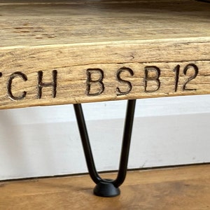 Puede incluir: Una mesa de madera con un acabado r&uacute;stico y patas de horquilla negras. La mesa tiene las palabras "BATCH BSB 12" talladas en la parte superior.