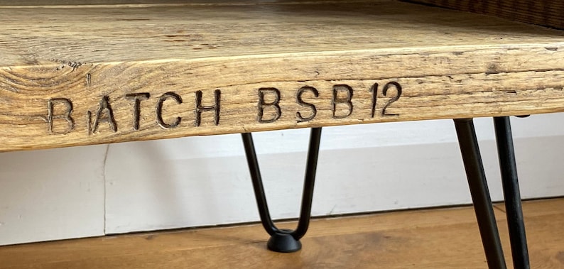 Puede incluir: Una mesa de madera con un acabado r&uacute;stico y patas de horquilla negras. La mesa tiene las palabras "BATCH BSB 12" talladas en la parte superior.