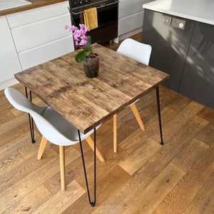 May include: A square wooden table with black hairpin legs and a light wood finish. The table is set with a white chair and a potted orchid with pink flowers.