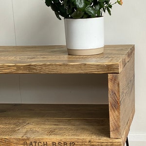 Puede incluir: Una estanter&iacute;a de madera r&uacute;stica con un solo estante y patas de horquilla negras. La estanter&iacute;a est&aacute; hecha de madera recuperada y tiene un acabado natural. Una planta en maceta con flores naranjas se coloca encima de la estanter&iacute;a. La estanter&iacute;a est&aacute; etiquetada como "BATCH BSB12".