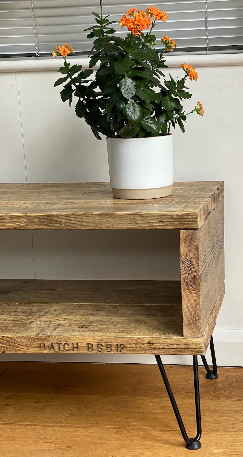 Puede incluir: Una estanter&iacute;a de madera r&uacute;stica con un solo estante y patas de horquilla negras. La estanter&iacute;a est&aacute; hecha de madera recuperada y tiene un acabado natural. Una planta en maceta con flores naranjas se coloca encima de la estanter&iacute;a. La estanter&iacute;a est&aacute; etiquetada como "BATCH BSB12".
