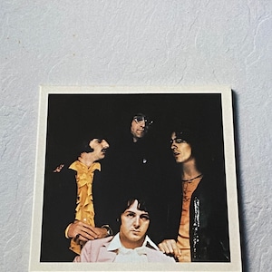 Könnte beinhalten: Albumcover für "The Beatles Rarities" mit einem Foto der Band. Der Titel ist in roter und schwarzer Schrift. Die Bandmitglieder tragen verschiedene Outfits, darunter einen rosa Blazer und ein gelbes Rüschenhemd. Der Hintergrund ist dunkel.
