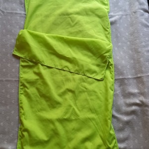 Könnte beinhalten: Ein leuchtend grüner Schlafsack aus leichtem Stoff. Der Schlafsack ist in der Hälfte gefaltet und liegt flach auf einer weißen Oberfläche.