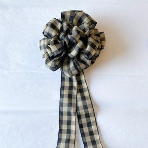 May include: A black and tan gingham bow with two long tails. The bow is made of a soft, textured fabric.