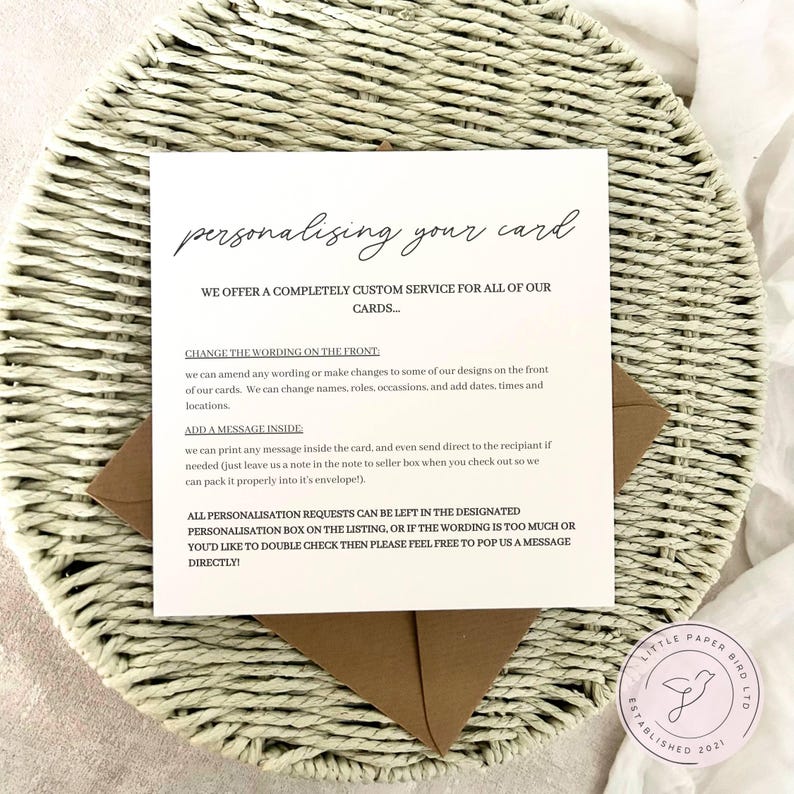 May include: A square white card with text, placed on a woven basket. The card reads "personalising your card" and details a custom service for cards, including wording changes and adding messages. A brown envelope is visible.