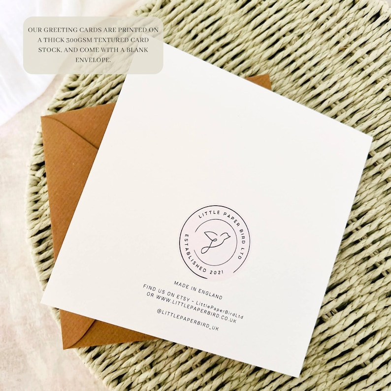May include: A white greeting card with a brown envelope, resting on a woven surface. The card features a circular logo with a bird design and the text "LITTLE PAPER BIRD LTD". Text on the card states the cards are printed on a thick textured card stock.